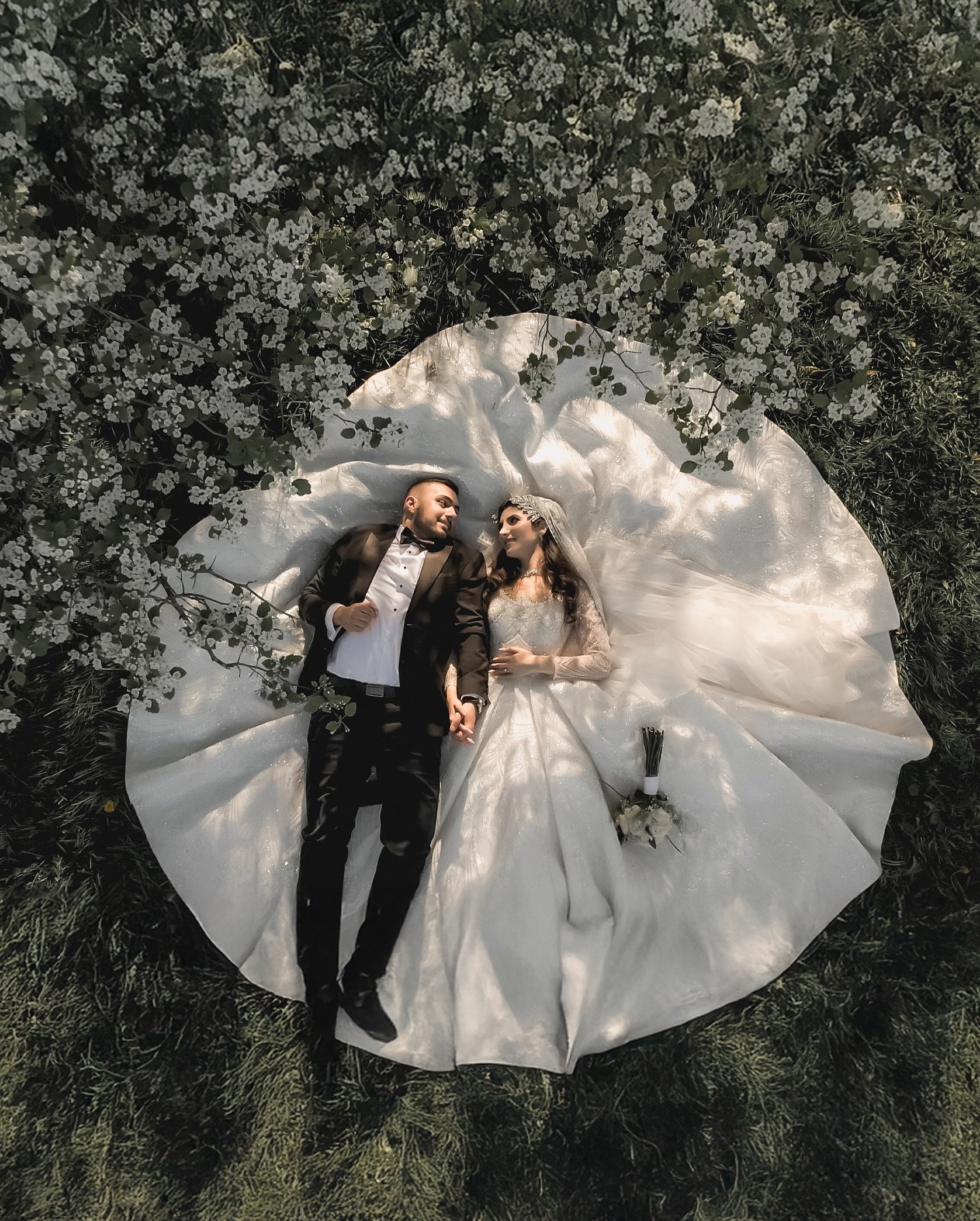 Seen from above, the couple lie on a carpet of white blossoms, her gown spread around them