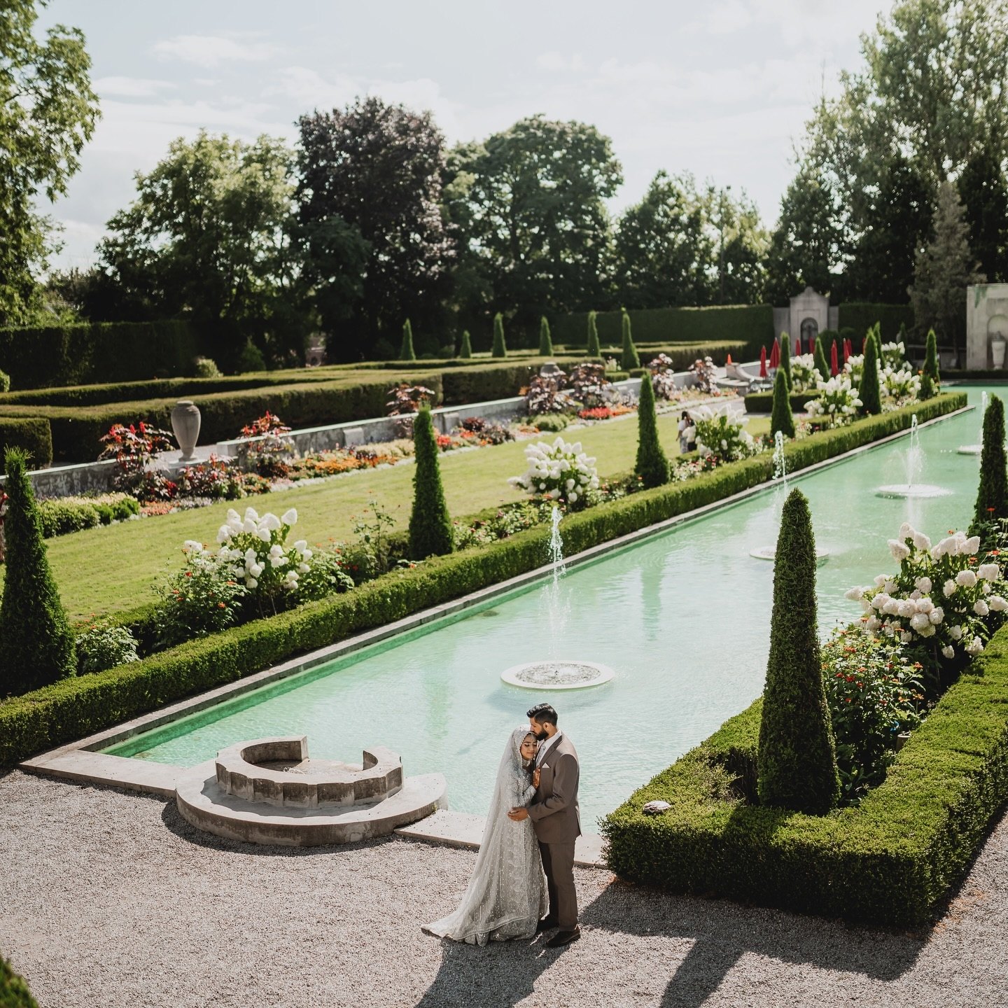 The couple beside a turquoise reflecting pool in a formal estate garden